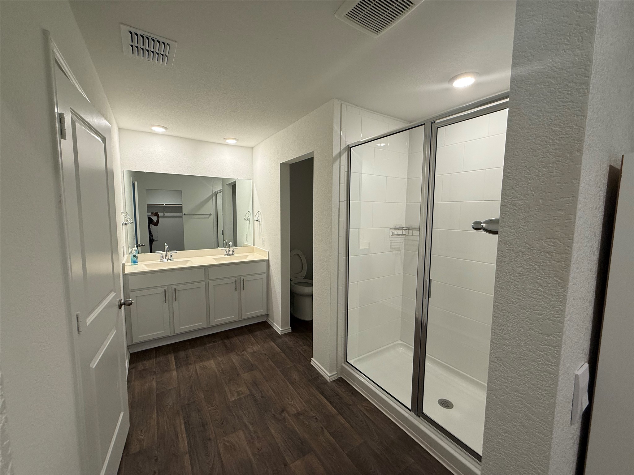 14812 Perlino Way Manor, Unit B Austin, TX 78721 - Photo 8 of 11 Bathroom featuring double vanity, a stall shower, dark wood finished floors, and a textured wall