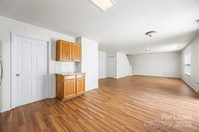 a view of empty room with wooden floor and kitchen