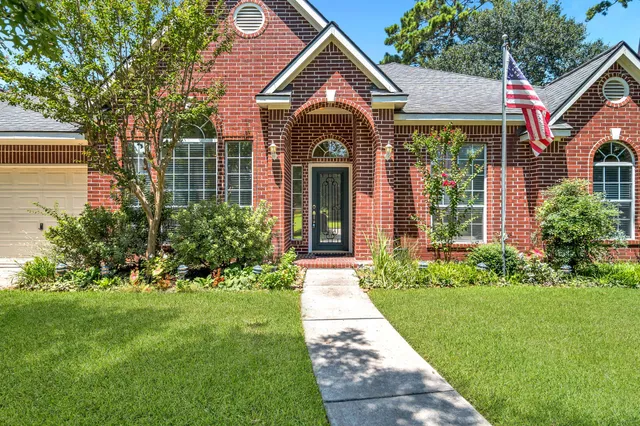 a view of a brick house with a large windows and a yard with plants and large trees
