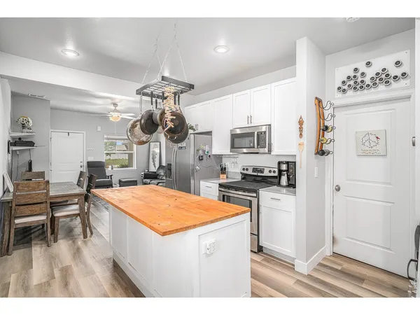 a kitchen with stainless steel appliances kitchen island granite countertop a refrigerator a stove a sink dishwasher and white cabinets with wooden floor
