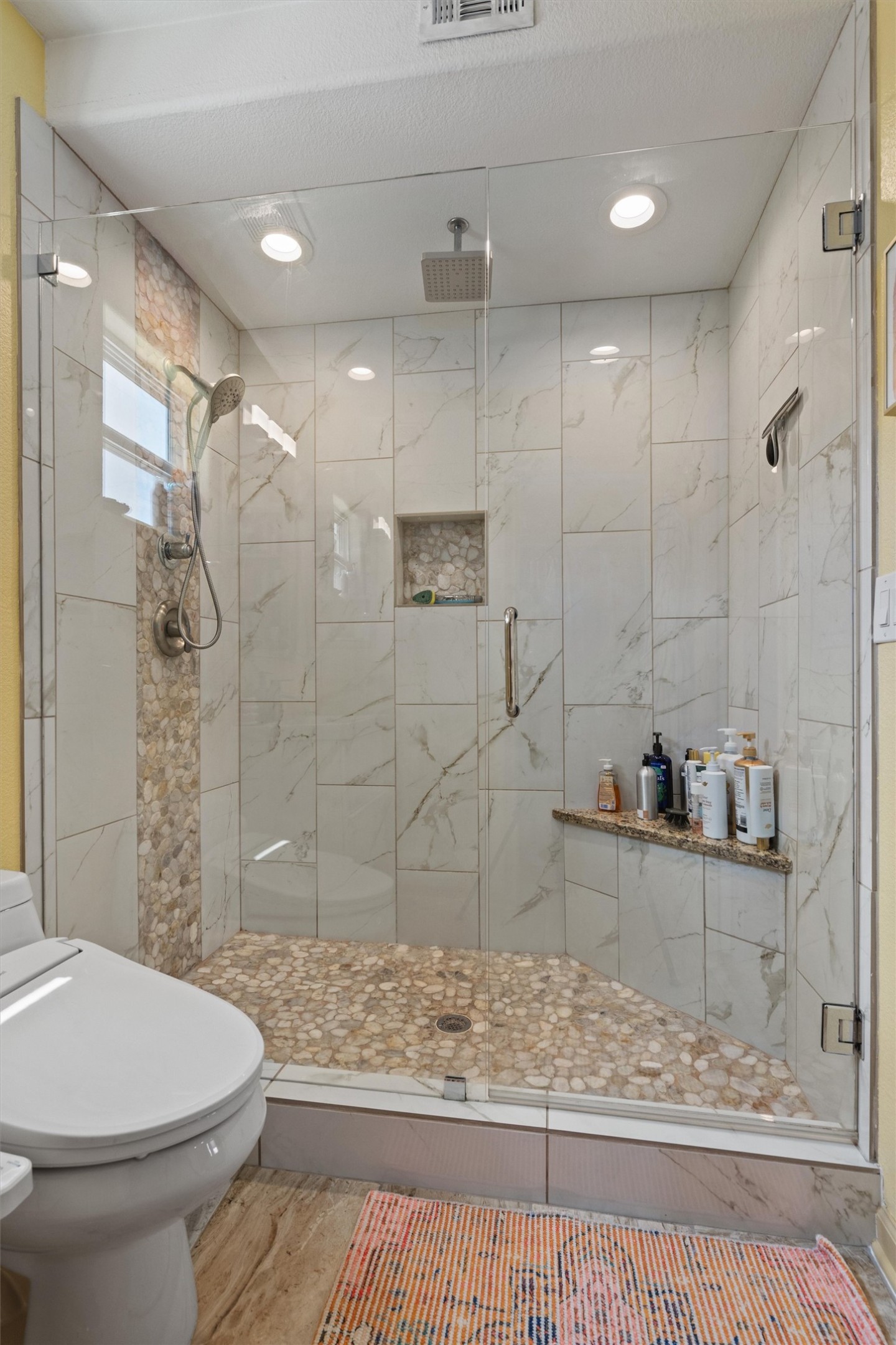1147 Webberville Road Austin, TX 78721 - Photo 25 of 37 A well-lit, tiled shower with a unique pebble floor offers a refreshing bathing experience.