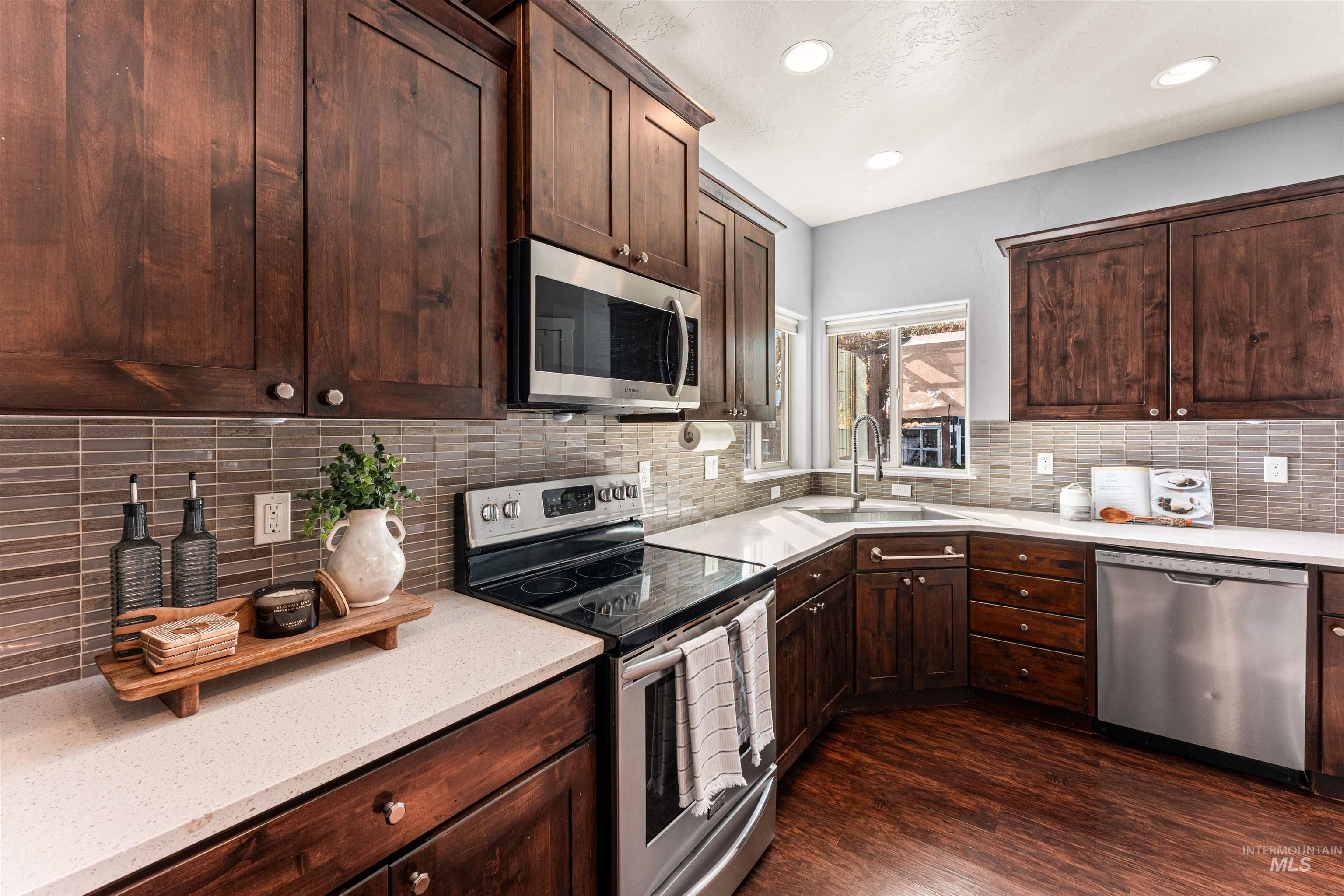 37 East Ensenada Drive Meridian, ID 83646 - Photo 9 of 46 Kitchen featuring stainless steel appliances, dark brown cabinets, tasteful backsplash, light stone counters, and dark wood-style flooring