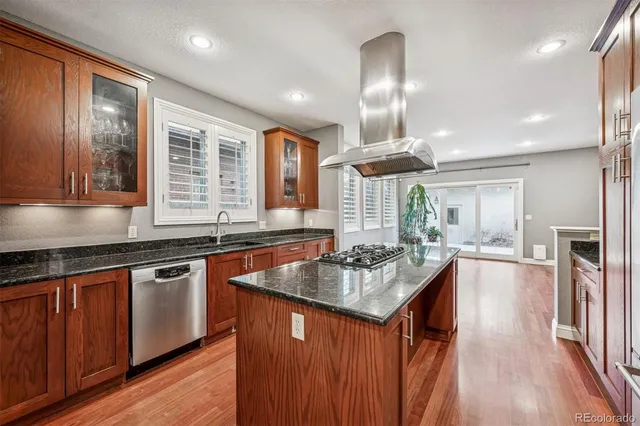 a kitchen with stainless steel appliances granite countertop a refrigerator a sink dishwasher a stove and white countertops with wooden floor