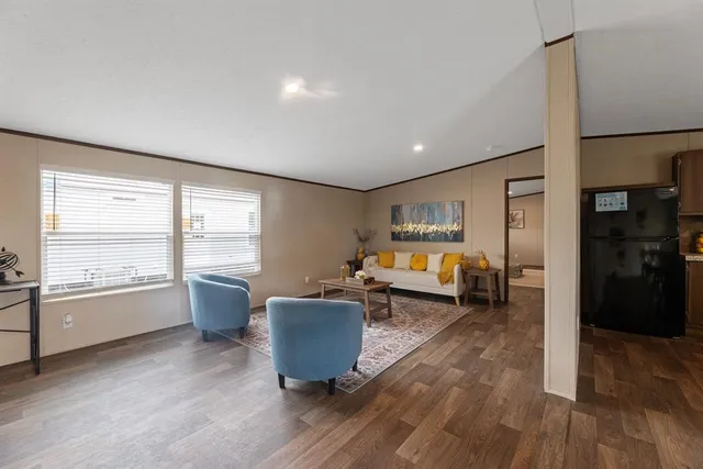 a living room with furniture two large window and wooden floor