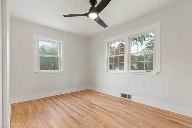 a view of empty room with wooden floor and fan