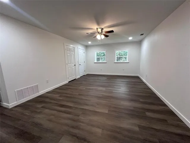 an empty room with wooden floor ceiling fan and windows