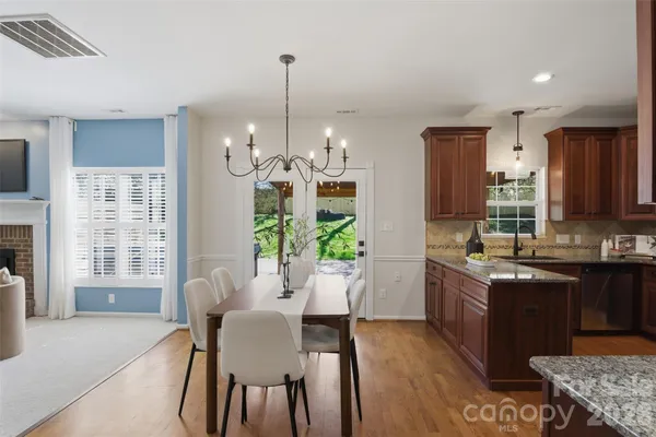 a open kitchen with stainless steel appliances granite countertop a refrigerator a sink dishwasher a dining table and chairs with wooden floor