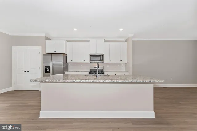 a kitchen with stainless steel appliances granite countertop a sink a stove a refrigerator and white cabinets with wooden floor