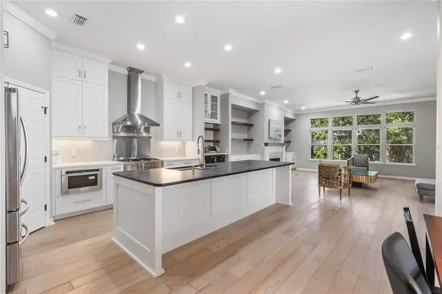 a kitchen with stainless steel appliances kitchen island granite countertop a stove a sink a refrigerator and white cabinets with wooden floor