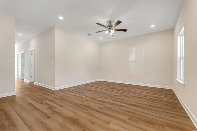 a view of an empty room with wooden floor and a ceiling fan