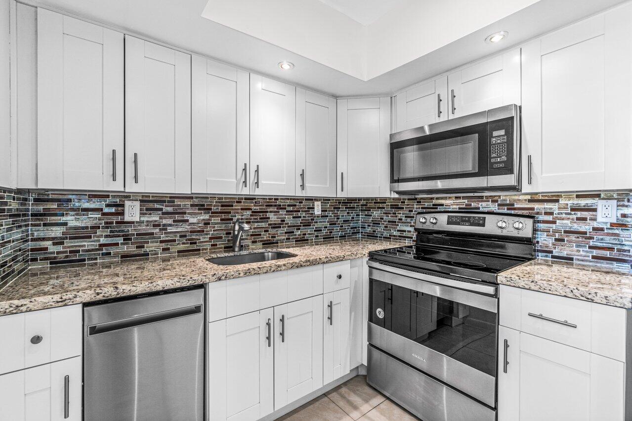 641 Normandy Lane, Unit N Delray Beach, FL 33484 - Photo 4 of 26 a kitchen with granite countertop white cabinets white stainless steel appliances and a sink