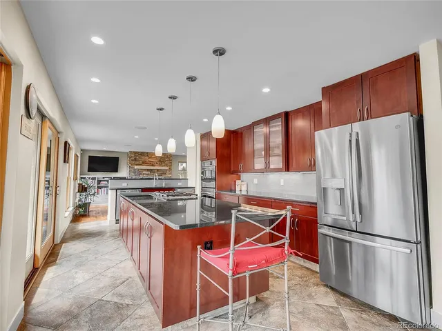 a kitchen with stainless steel appliances kitchen island granite countertop a refrigerator a stove a sink a dining table and chairs with wooden floor
