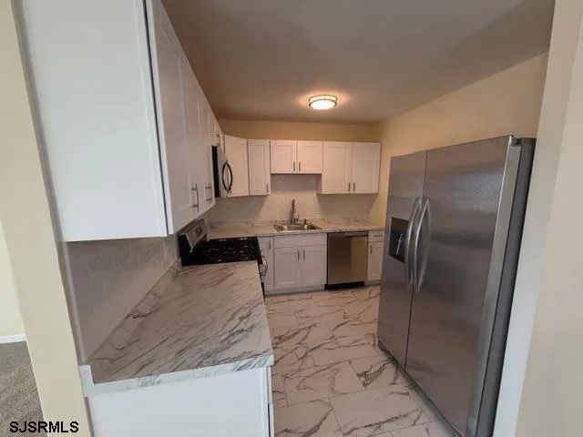 a kitchen with stainless steel appliances granite countertop a refrigerator a sink a stove a washer dryer and a refrigerator