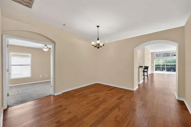 an empty room with wooden floor chandelier and windows