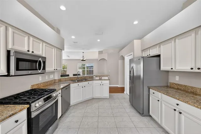a large kitchen with stainless steel appliances granite countertop a stove top oven a refrigerator and white cabinets
