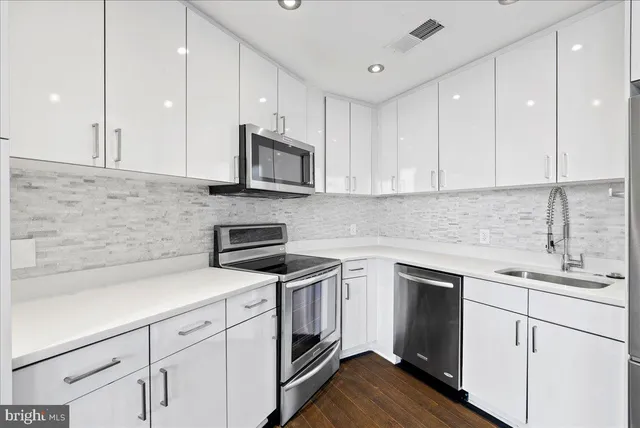a kitchen with cabinets stainless steel appliances a sink and wooden floor