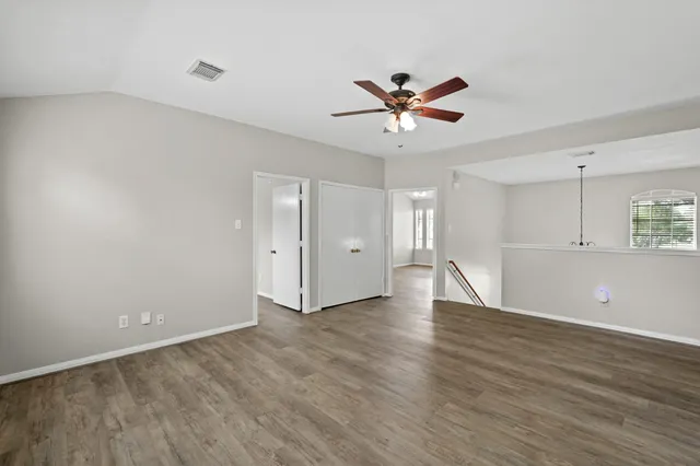 a view of an empty room with wooden floor and a ceiling fan