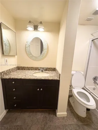 a bathroom with a granite countertop toilet sink and mirror