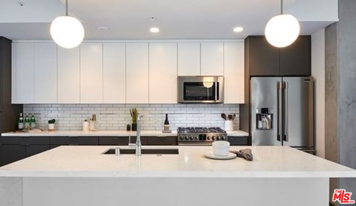 732 South Spring Street, Unit 918 Los Angeles, CA 90014 - Photo 3 of 31 a kitchen with stainless steel appliances kitchen island granite countertop a sink and a stove top oven with wooden floor