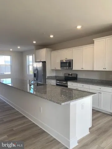 a kitchen with stainless steel appliances granite countertop a stove a sink a refrigerator white cabinets and a wooden floor