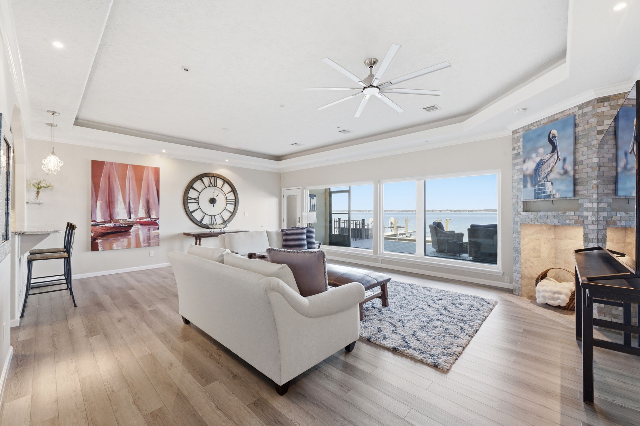 2 Regency Point Conroe, TX 77356 - Photo 5 of 44 Spacious living area with tray ceilings, wood-look flooring, and a striking fireplace enclave, all framed by expansive windows with stunning open water views.