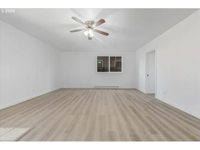 an empty room with wooden floor chandelier fan and windows