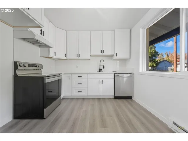 a kitchen with stainless steel appliances granite countertop a stove a sink and white cabinets with wooden floor