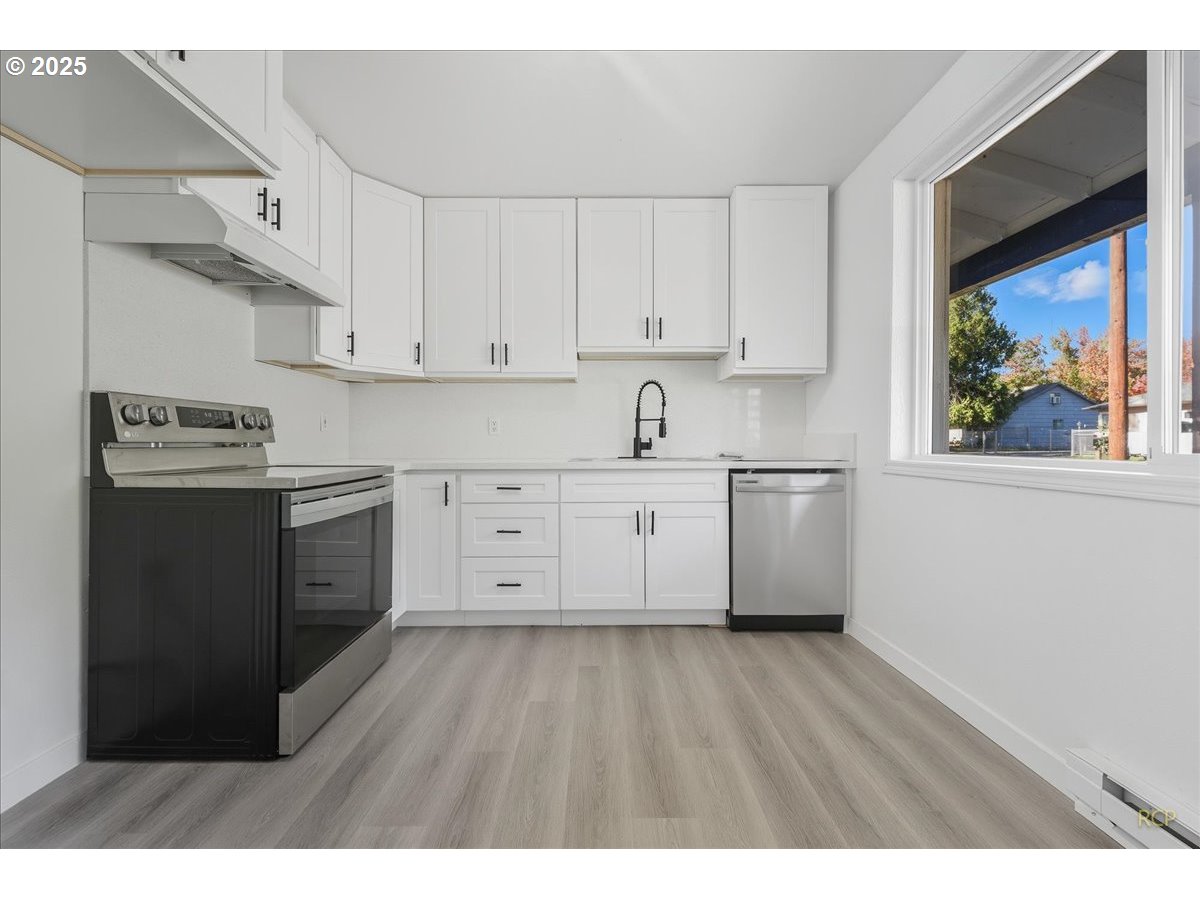 11420 Southeast Clinton Street Portland, OR 97266 - Photo 7 of 34 a kitchen with stainless steel appliances granite countertop a stove a sink and white cabinets with wooden floor