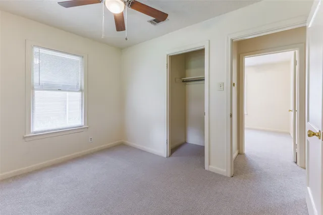 an empty room with chandelier fan and windows
