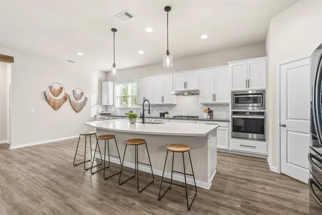 a kitchen with stainless steel appliances granite countertop a kitchen island a stove a refrigerator a sink a dining table and chairs with wooden floor