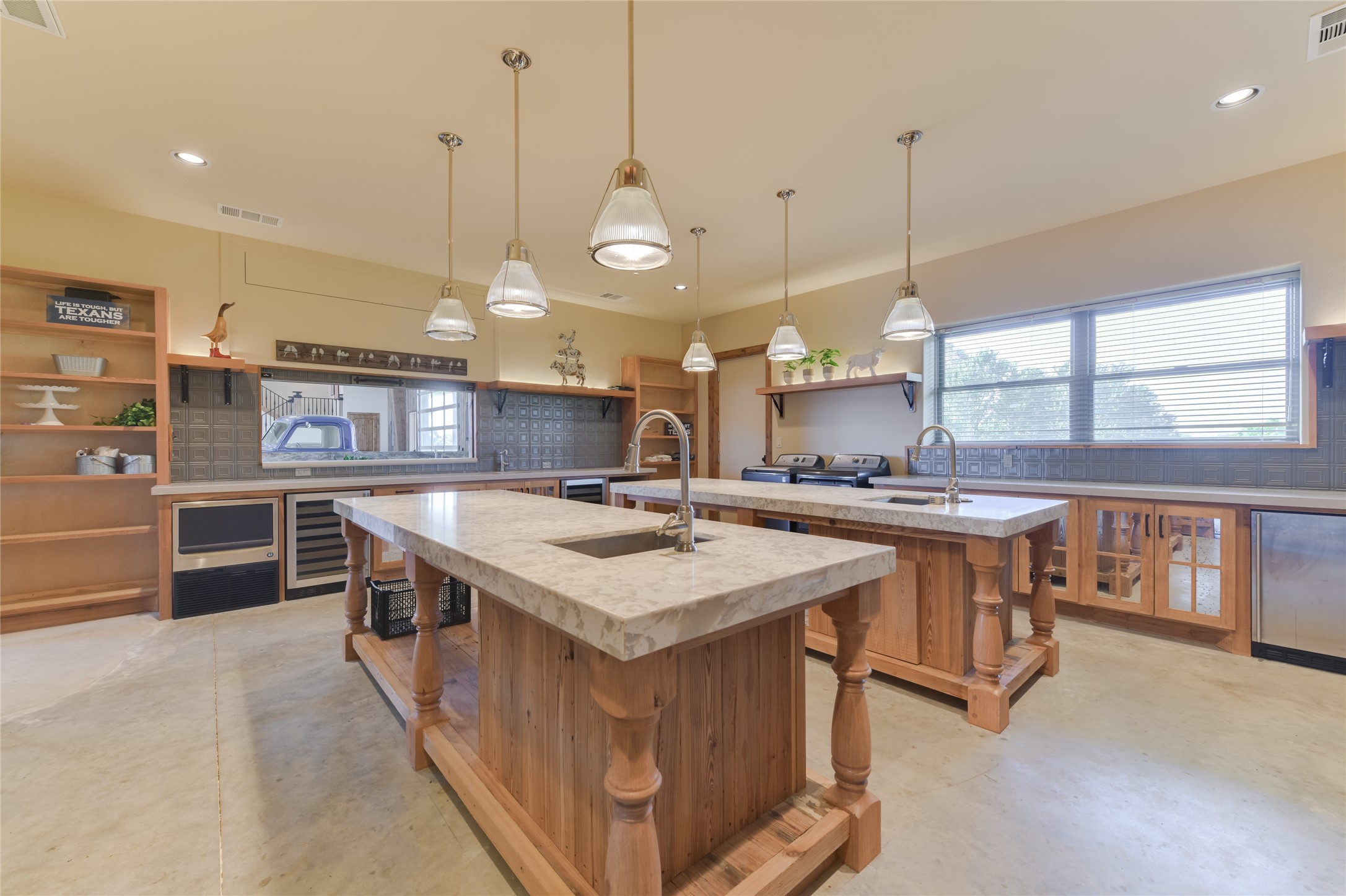 21729 Farm To Market 1887 Hempstead, TX 77445 - Photo 33 of 49 View of the building's commercial KITCHEN - opening to the Bar area - includes concrete flooring, 2 center islands with sinks/stone counters/overhead lighting fixtures, built-in wood shelving, Hushizaki stainless ice maker, W/D connection area, GE stainless wine chiller, 2 stainless GE dishwashers, GE stainless mini refrigerator, GE Stainless microwave, GE 6 burner gas/griddle range with two ovens below, Zephyr vent hood with decorative copper and wood surround.