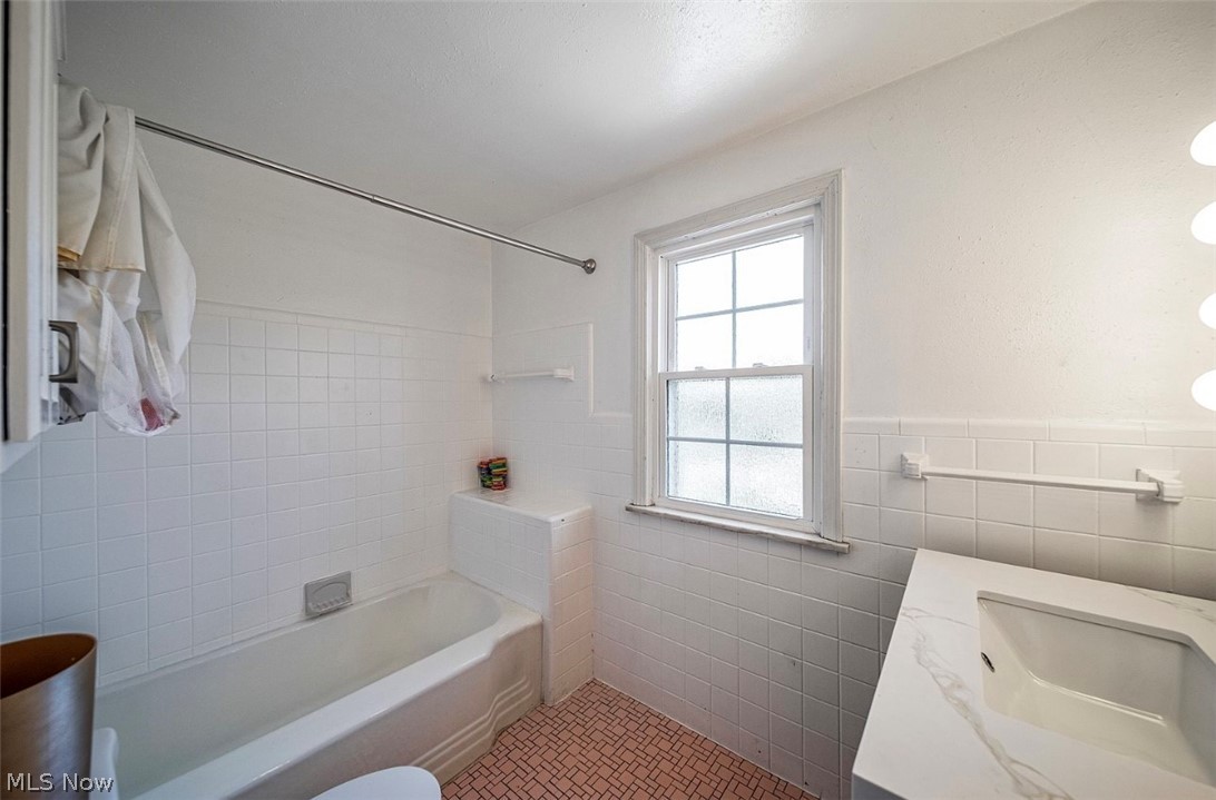 4069 Bushnell Road Cleveland, OH 44121 - Photo 18 of 39 Bathroom with vanity, shower / bath combination with curtain, tile walls, light tile patterned flooring, and a wainscoted wall