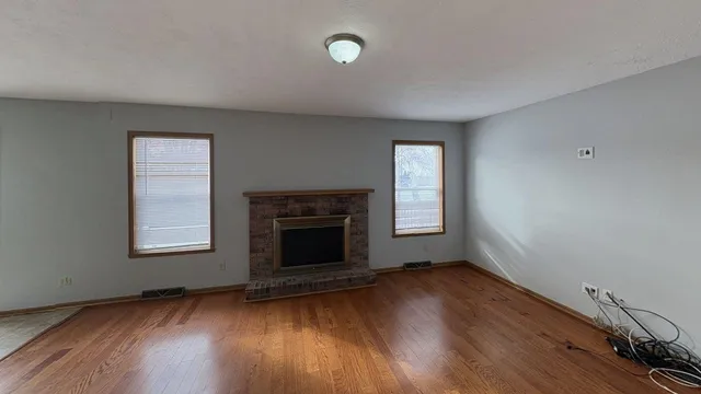 an empty room with wooden floor fireplace and windows