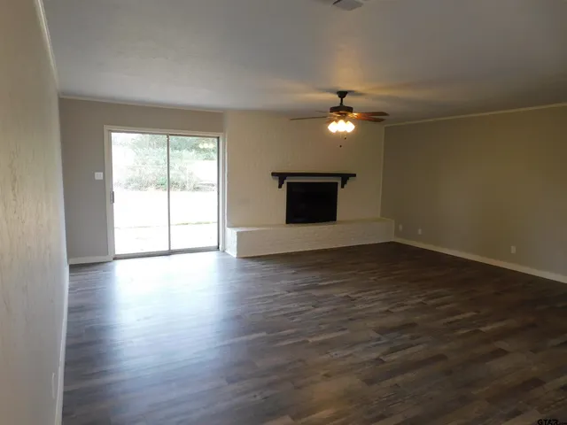 an empty room with wooden floor chandelier fan and windows