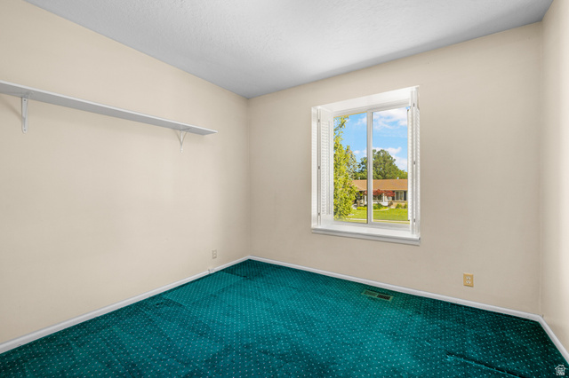 2088 Falcon Way Sandy, UT 84093 - Photo 18 of 46 Room featuring a white-framed window with louvered shutters, light beige walls, and teal patterned carpeting