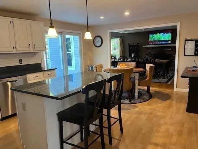 a kitchen with stainless steel appliances granite countertop a stove top oven a sink a dining table and chairs with wooden floor