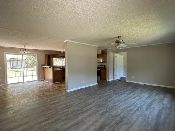 an empty room with wooden floor kitchen view and a window