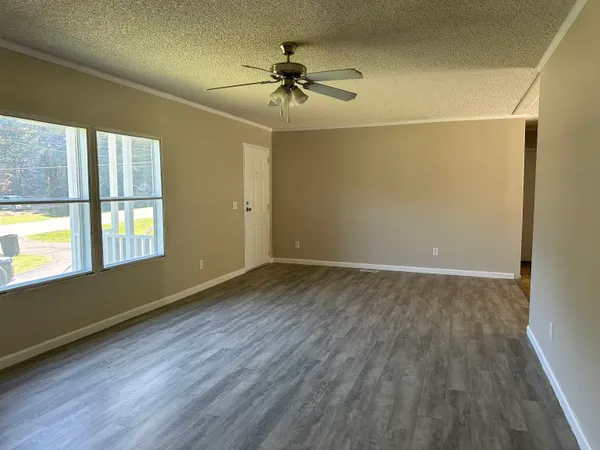 an empty room with wooden floor fan and windows