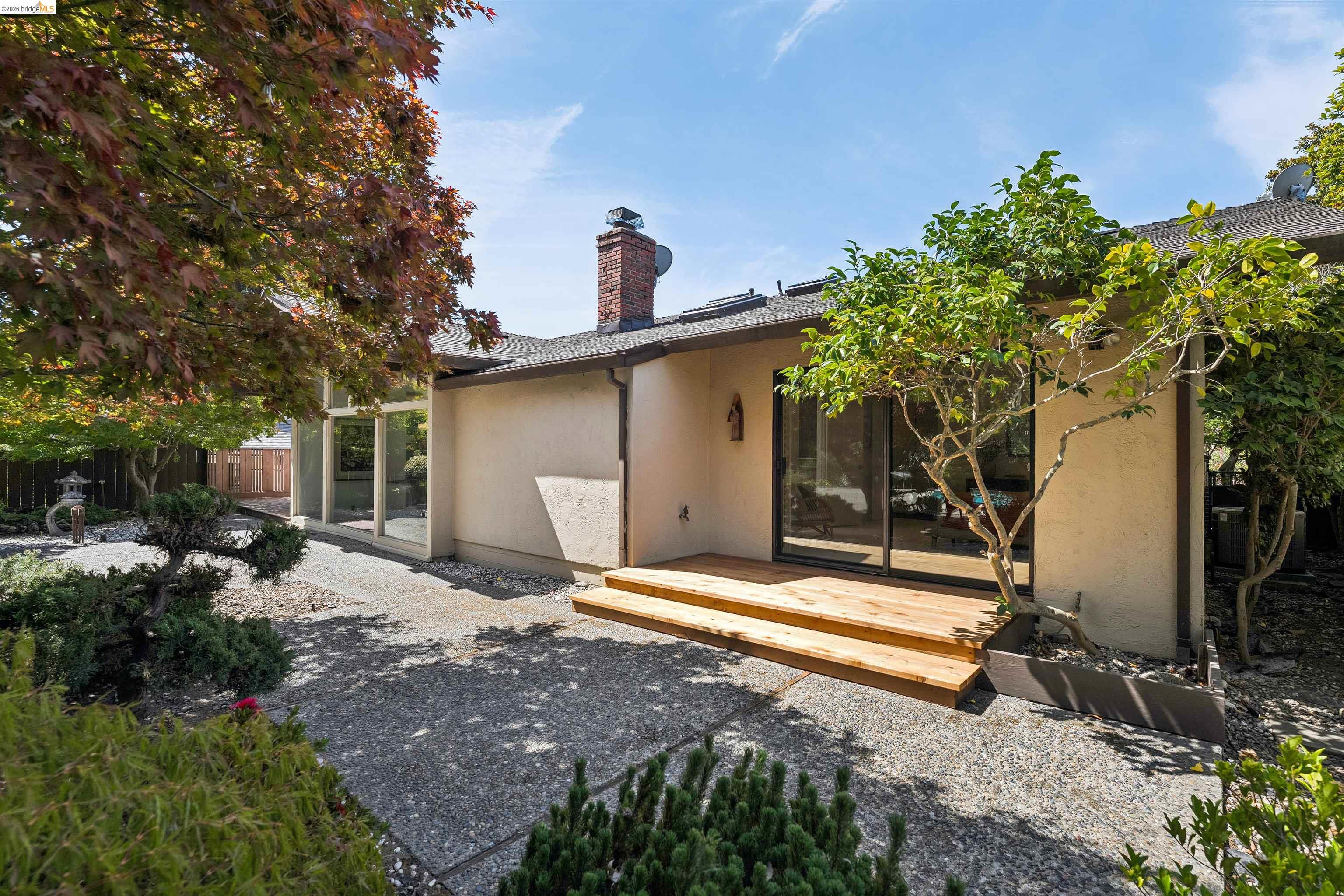 7 Jo Lin Court El Sobrante, CA 94803 - Photo 85 of 99 Exterior stucco finish with a prominent brick chimney, multiple sliding glass doors, a wooden deck, and a gravel patio area