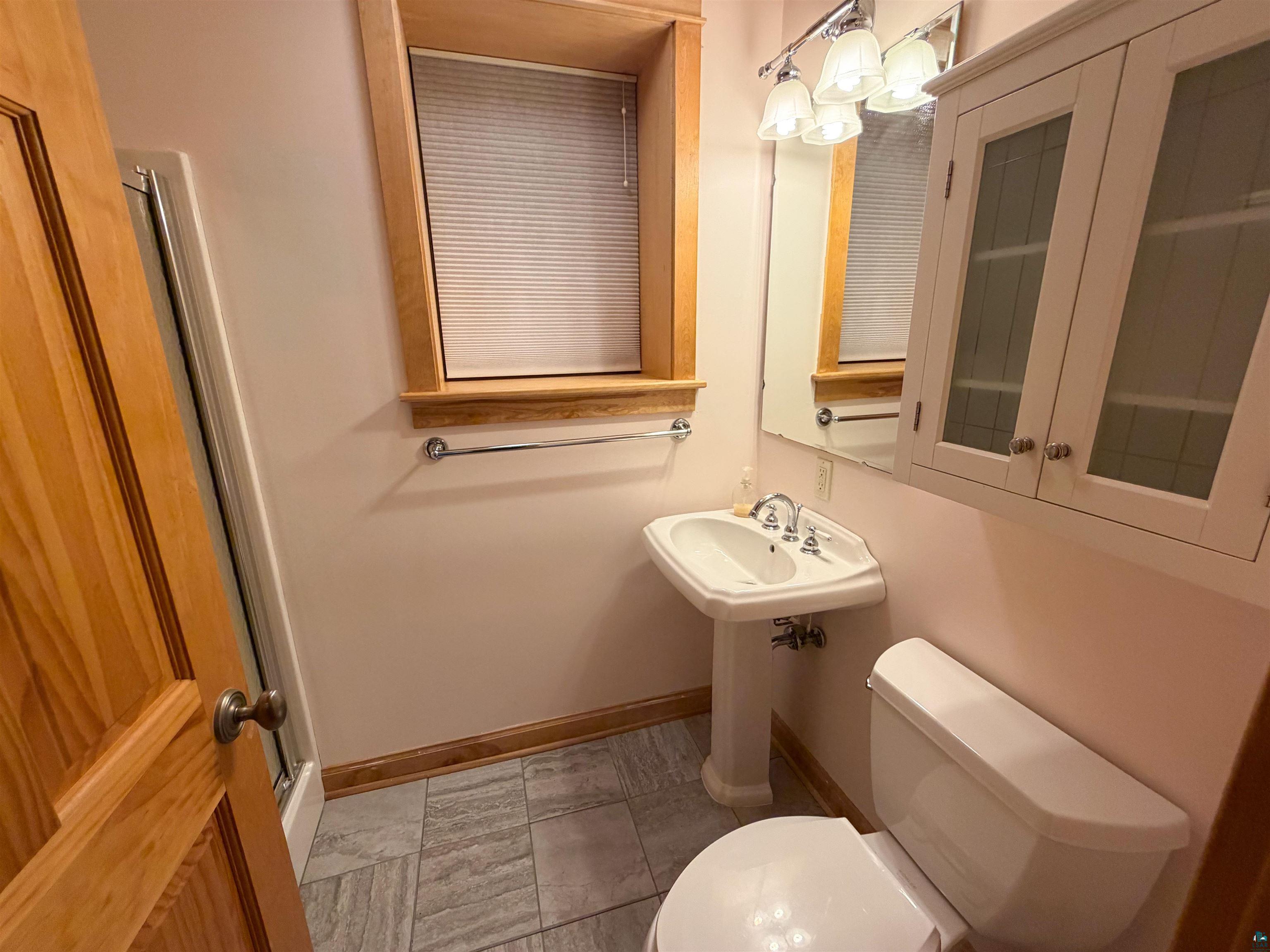 13 West 8th Street Duluth, MN 55806 - Photo 46 of 57 Pedestal sink with chrome fixtures, wood-framed window, and a built-in wall cabinet with glass doors