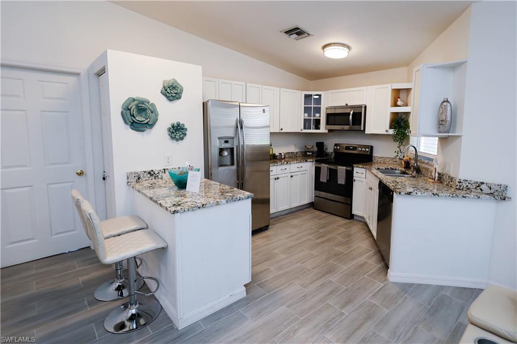 650 103rd Avenue North Naples, FL 34108 - Photo 4 of 13 a kitchen with stainless steel appliances granite countertop a stove top oven a refrigerator a sink dishwasher and a dining table with wooden floor