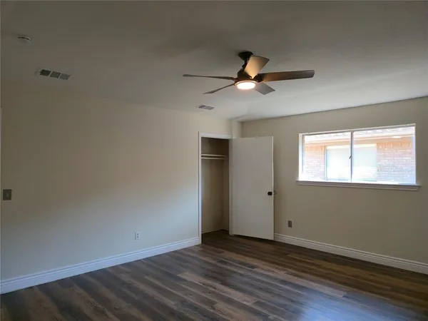 an empty room with wooden floor fan and windows