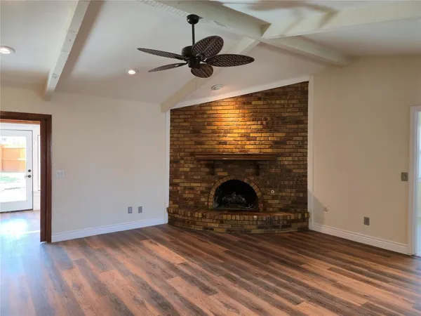 a view of an empty room with wooden floor a fireplace and a window