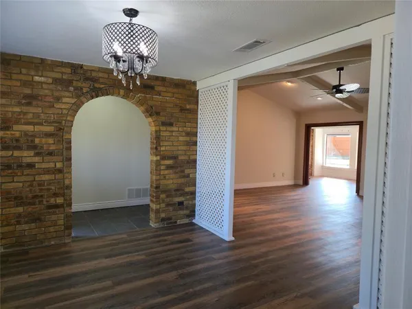 an empty room with wooden floor chandelier and windows
