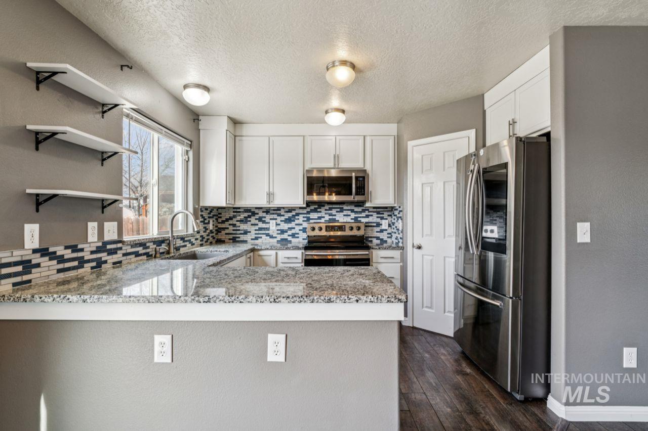 5410 Barkley Way Caldwell, ID 83607 - Photo 15 of 50 Kitchen featuring stainless steel appliances, light stone counters, tasteful backsplash, a peninsula, and open shelves