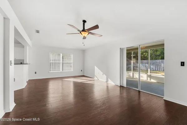an empty room with wooden floor ceiling fan and windows