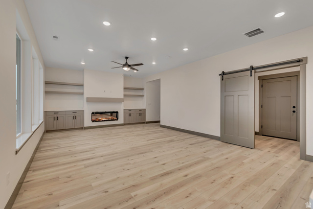 3317 South 1000 West, Unit 6010 Logan, UT 84321 - Photo 13 of 34 Unfurnished living room with a barn door, a glass covered fireplace, recessed lighting, built in features, and light wood-style floors