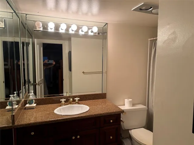 a bathroom with a granite countertop sink vanity mirror and toilet