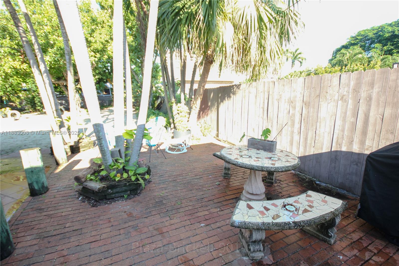 2754 Southwest 36th Avenue Miami, FL 33133 - Photo 24 of 35 This outdoor area features a brick-paved space surrounded by greenery, ideal for dining, gatherings, or simply enjoying nature, with a unique stone table and ample seating for comfort.