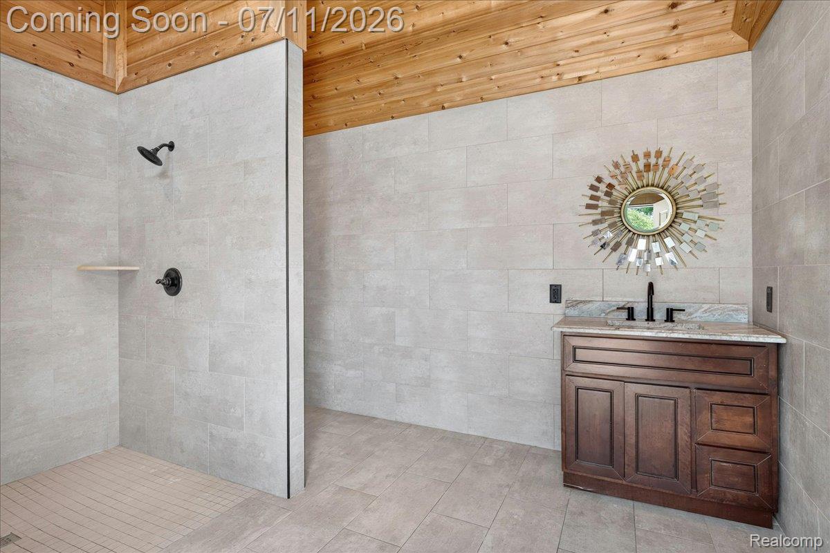23750 East River Road Grosse Ile, MI 48138 - Photo 40 of 54 Spacious bathroom featuring a walk-in shower with matte black fixtures, a wooden plank ceiling, light-toned tile flooring, and a dark wood vanity with a stone countertop